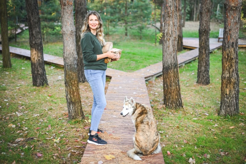 A woman carrying firewood with her dog next to her